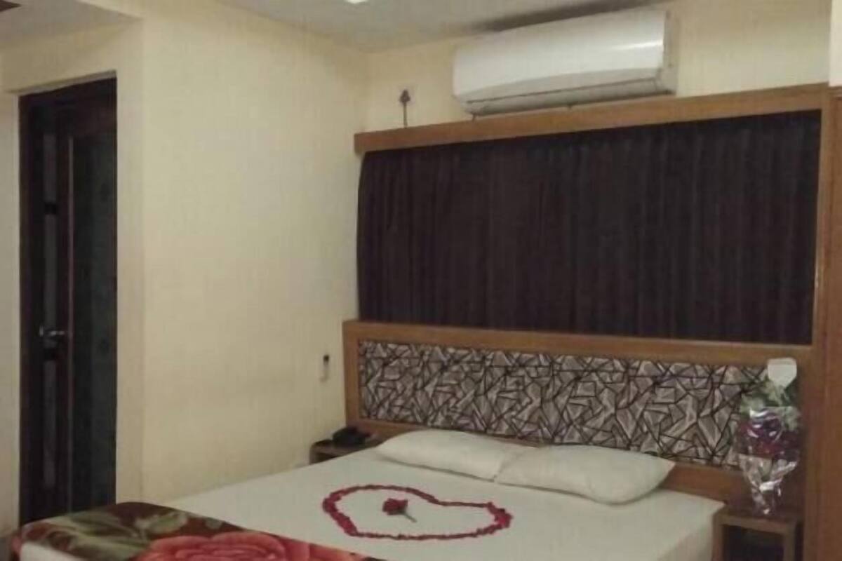 Una habitación de hotel con una cama, una mesita de noche, aire acondicionado y una puerta.