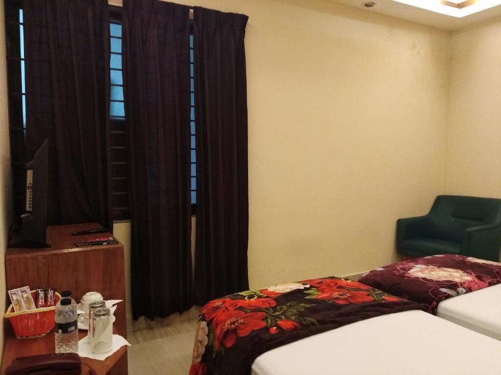 A hotel room with a bed, a desk with a telephone and a basket of items, a chair, and a window with curtains.
