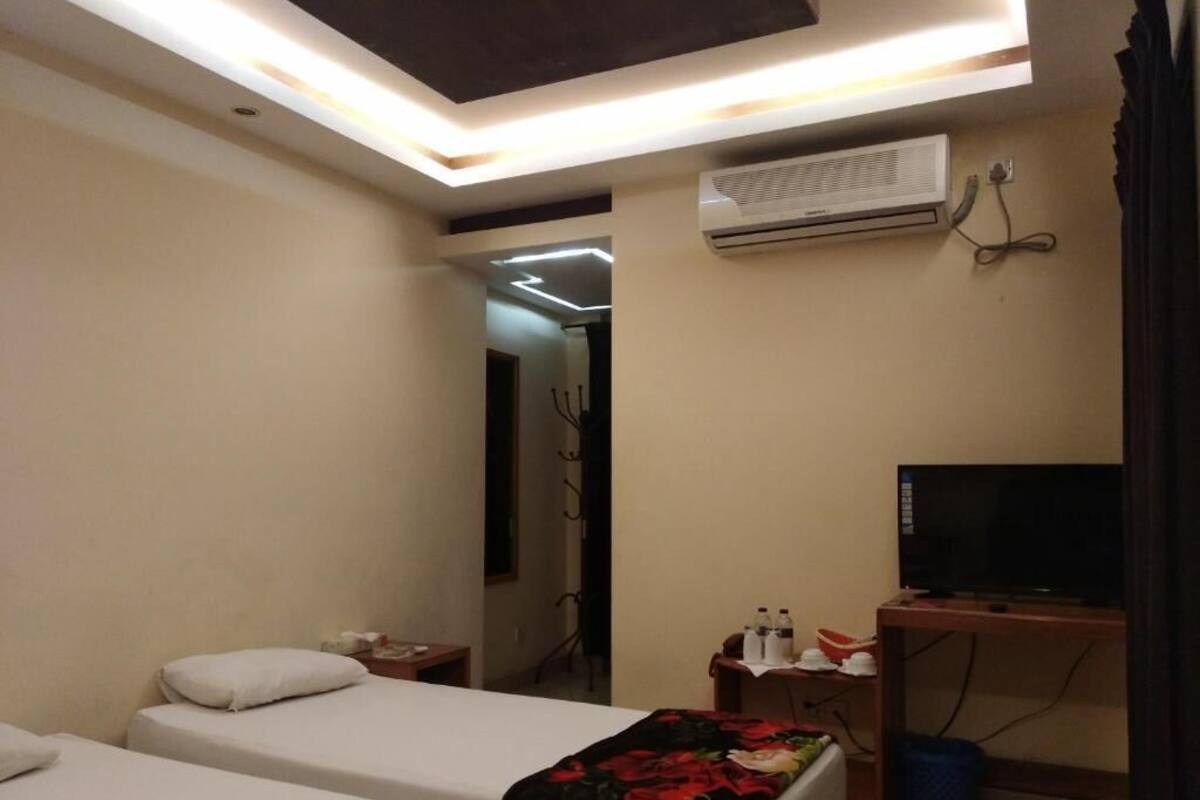 Habitación de hotel con dos camas, un escritorio con televisor, un equipo de aire acondicionado y un espejo en la pared.