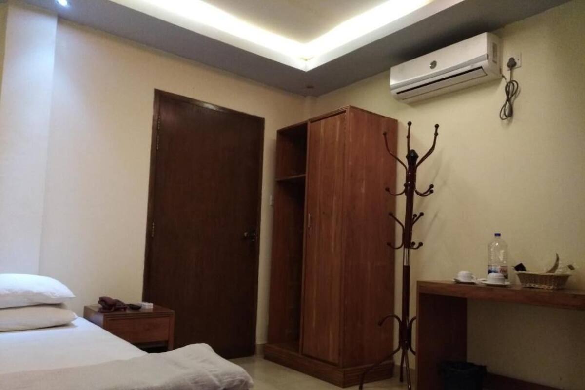 Un dormitorio con cama, armario, perchero, escritorio con silla y unidad de aire acondicionado.