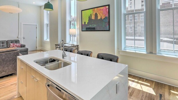 Una cucina moderna con isola centrale, luci a sospensione e ampie finestre che offrono vista sulla città.