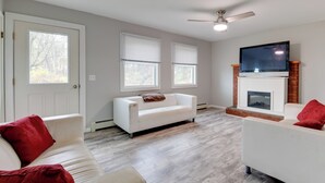 A living room with a white sofa, red cushions, a fireplace, and a ceiling fan. - Ski, Hike & Explore: Home 5 Mi to Dtwn Burlington! (Essex Junction)