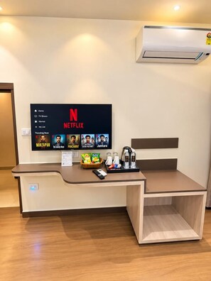 A hotel room with a desk, a mounted TV displaying Netflix, and a coffee station. - Hotel Vedic Roots (Varanasi)