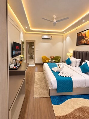 A modern hotel room with a bed, bedside table, TV, and a ceiling fan. - Hotel Vedic Roots (Varanasi)