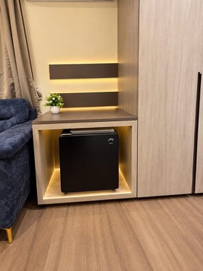 A compact kitchenette with a built-in refrigerator, a small countertop, and a potted plant. - Hotel Vedic Roots (Varanasi)