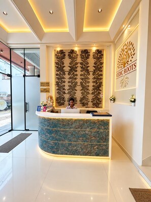 A reception desk with a floral pattern, a wall-mounted sign reading 'Vedic Roots', and a check-in/out schedule. - Hotel Vedic Roots (Varanasi)