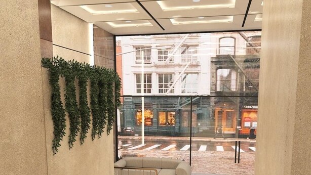 A modern interior with a sofa and a radiator, a glass wall with a view of the street, and a plant decoration. - Hotel Vedic Roots (Varanasi)