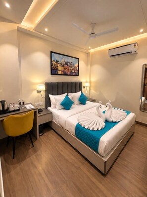 A hotel room with a bed, a desk, a chair, a ceiling fan, and an air conditioning unit. - Hotel Vedic Roots (Varanasi)