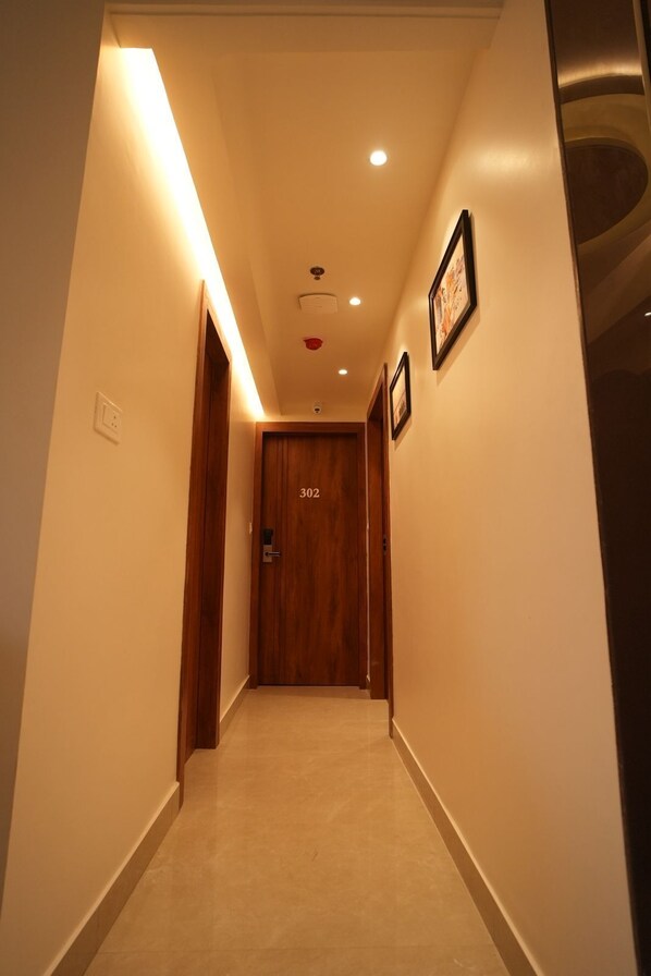 A hallway with a wooden door labeled '302', recessed lighting, and framed pictures on the wall. - Hotel Vedic Roots (Varanasi)