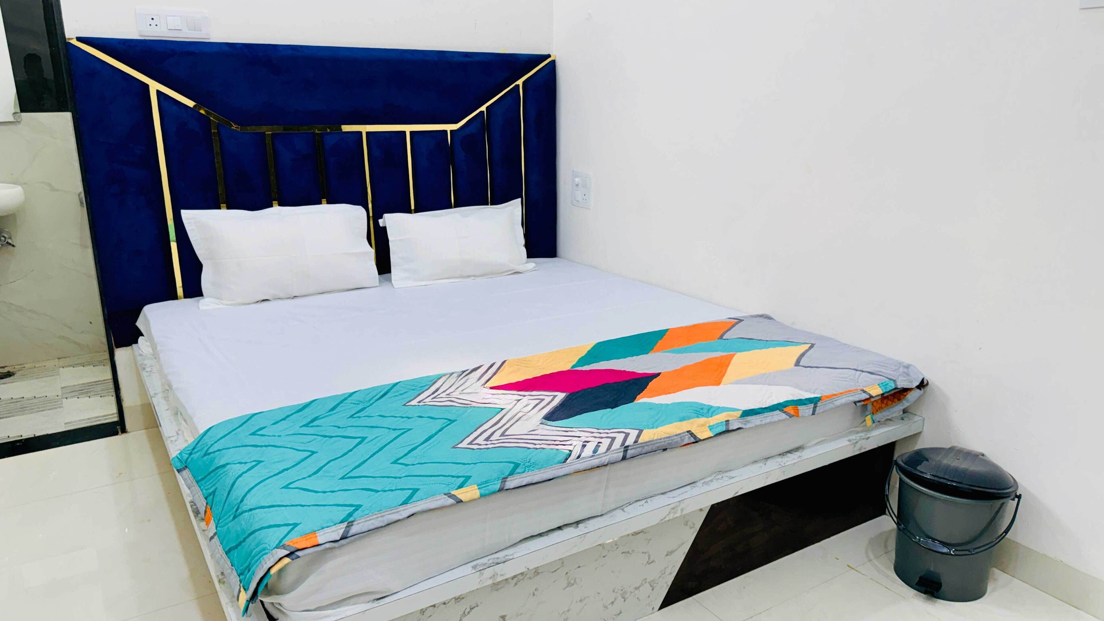A bed with a blue headboard, white bedding, and a colorful geometric-patterned blanket.