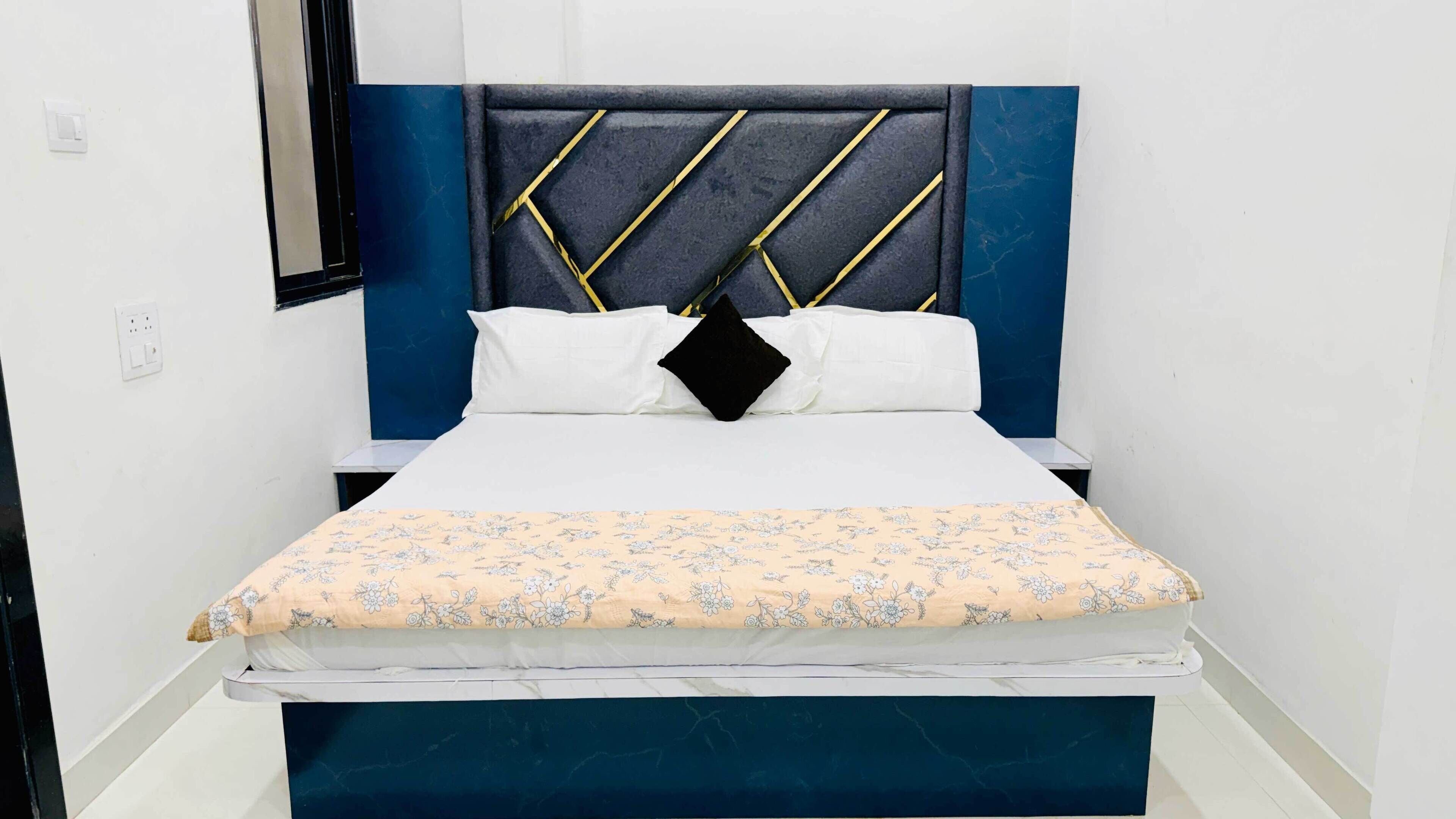 A bed with a patterned bedspread, a headboard with a geometric design, and a bedside table.