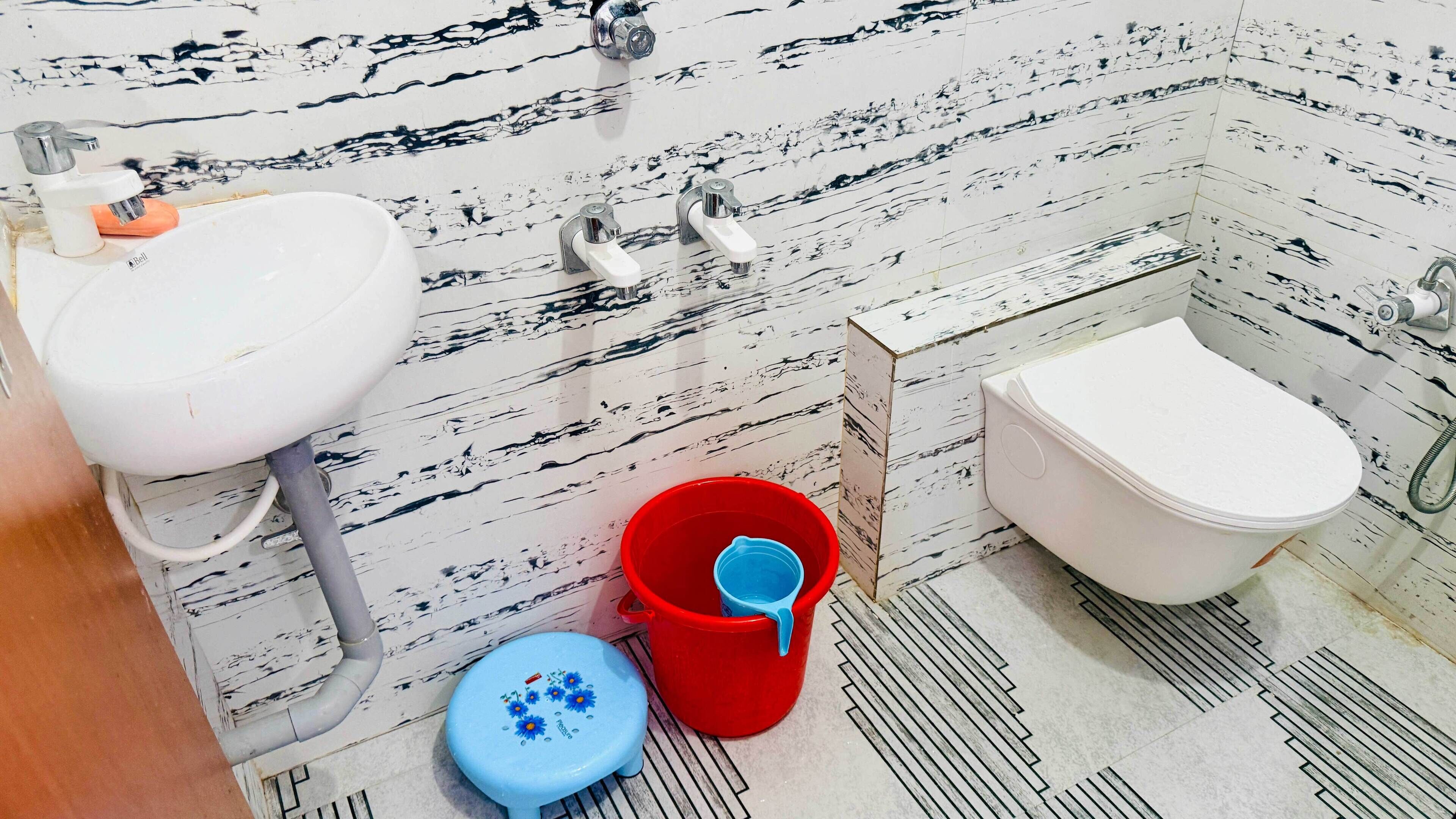 Ein Badezimmer mit einem weißen Waschbecken, einer Toilette und einem roten Eimer.