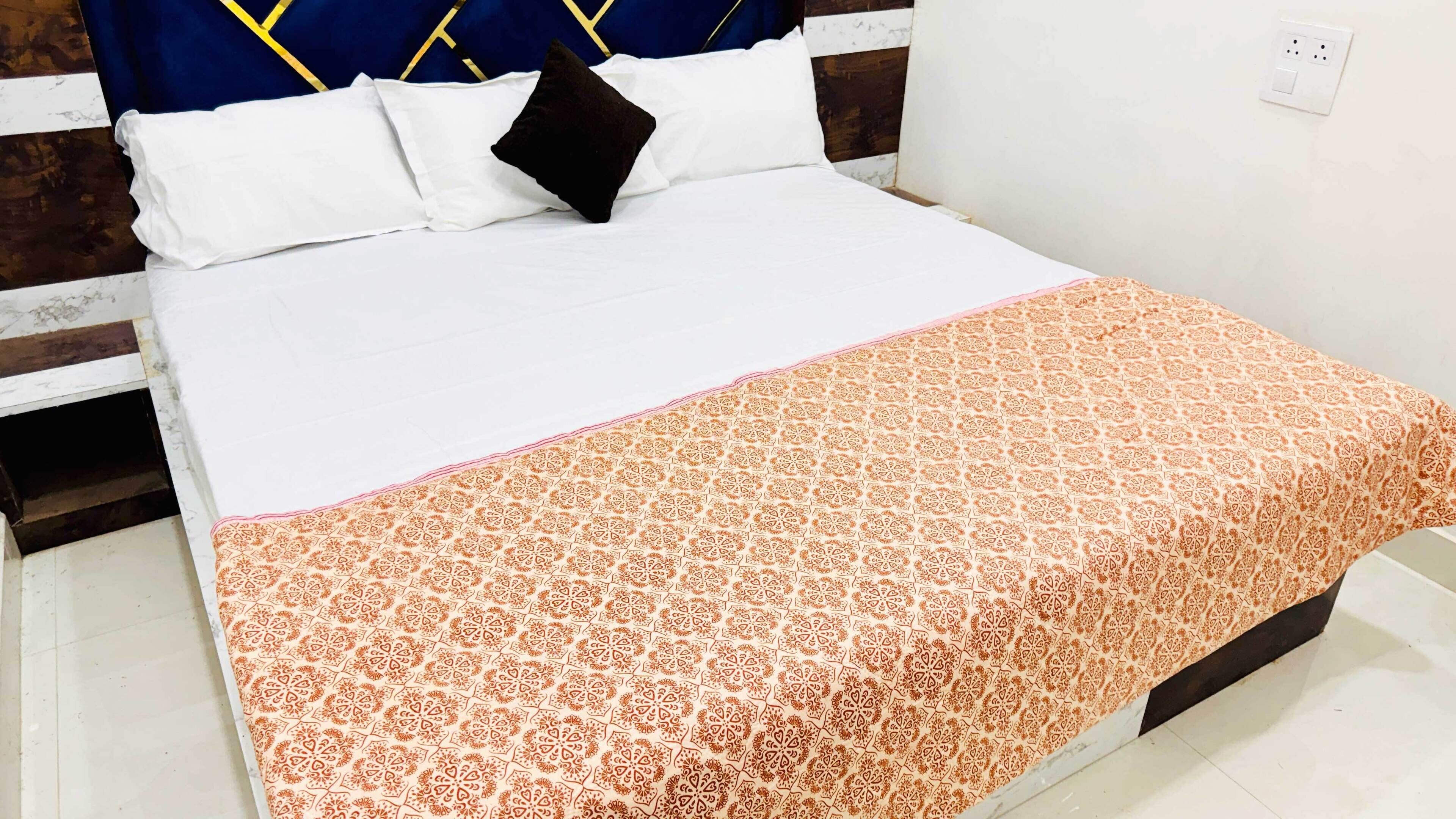 A neatly made bed with white linens and a patterned orange blanket.