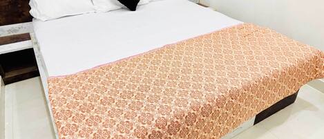 A neatly made bed with white linens and a patterned orange blanket.