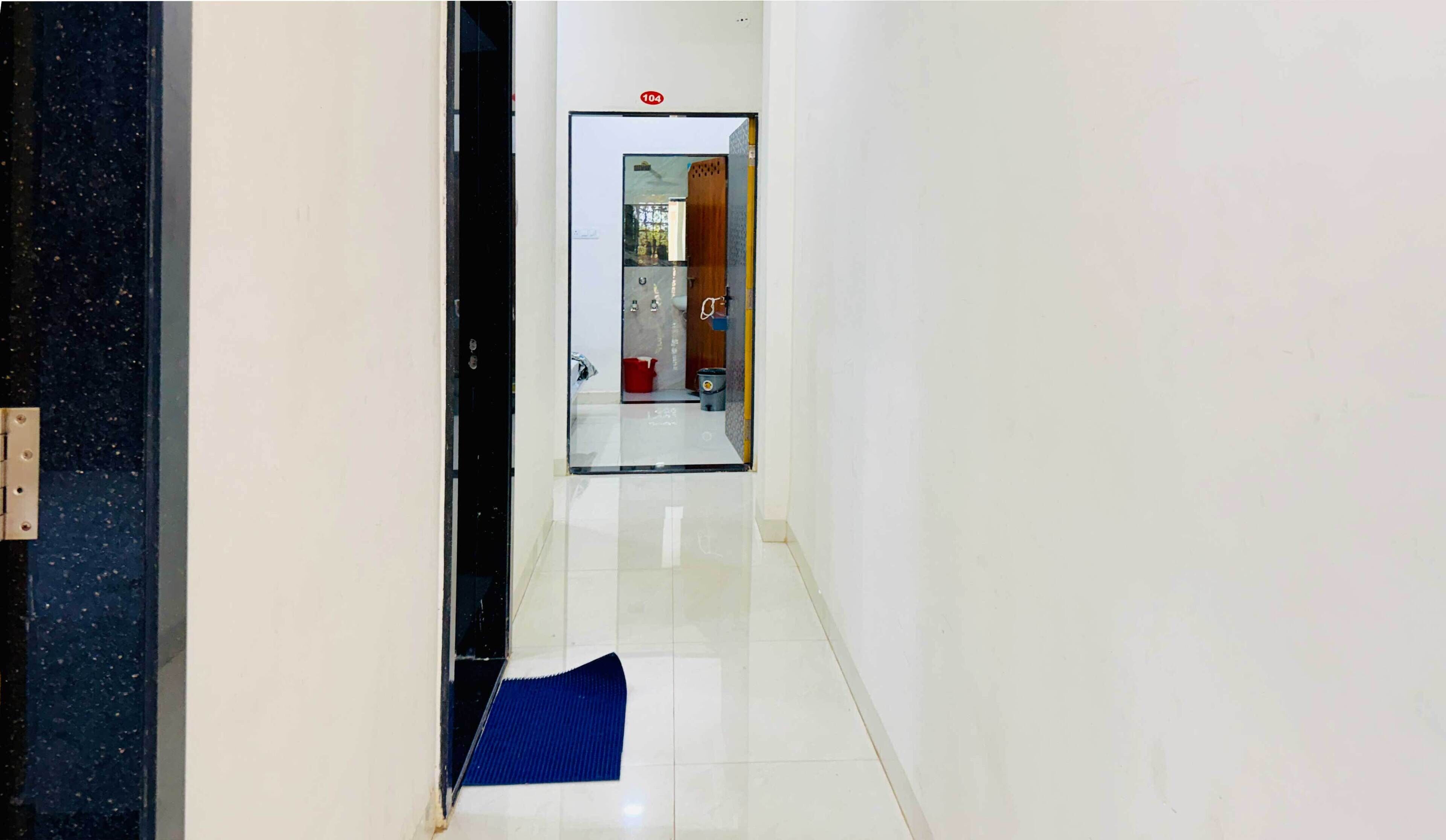 A hallway with a blue mat at the end, a door with a number sign, and a glimpse of a room with a sink and cabinets.