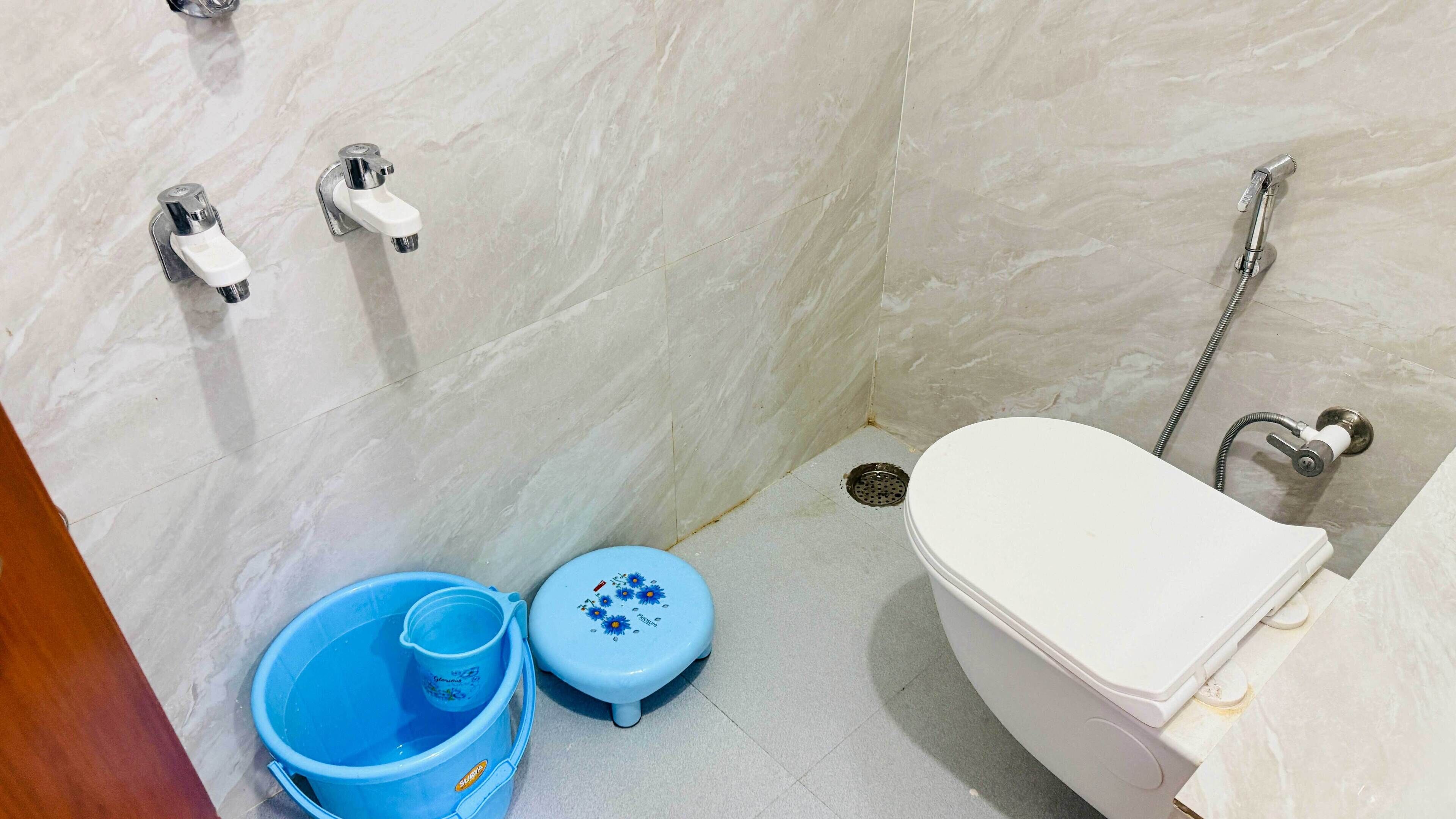 A small bathroom with a white toilet, a shower, and two blue buckets.