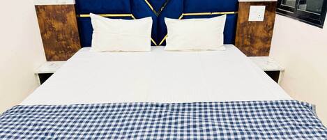 Una cama con colcha a cuadros, cabecero azul con adornos dorados y almohadas blancas.