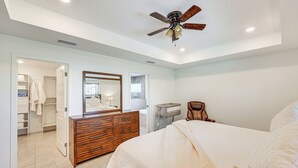 A bedroom with a bed, a wooden dresser, a mirror, and a ceiling fan. - Heated Pool & Outdoor Kitchen: Cape Coral Home (Cape Coral)