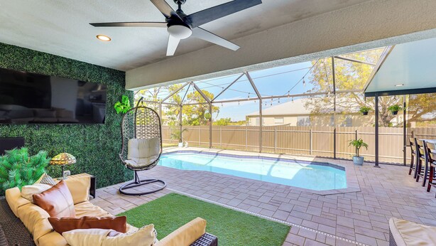 A modern outdoor living area with a pool, comfortable seating, and a ceiling fan. - Heated Pool & Outdoor Kitchen: Cape Coral Home (Cape Coral)