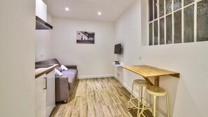 Una cocina compacta con una mesa de madera, dos taburetes, un sofá y un televisor fijado a la pared.