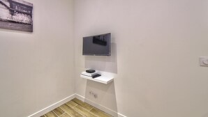 Un baño pequeño y moderno con televisor montado, una estantería con control remoto y suelo de madera.