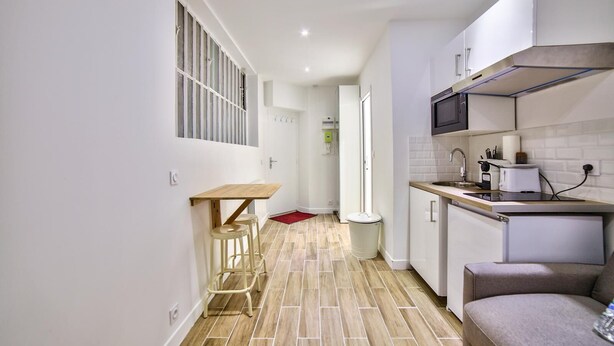 Una cocina compacta con una mesa de madera y taburetes, un microondas y un refrigerador pequeño.
