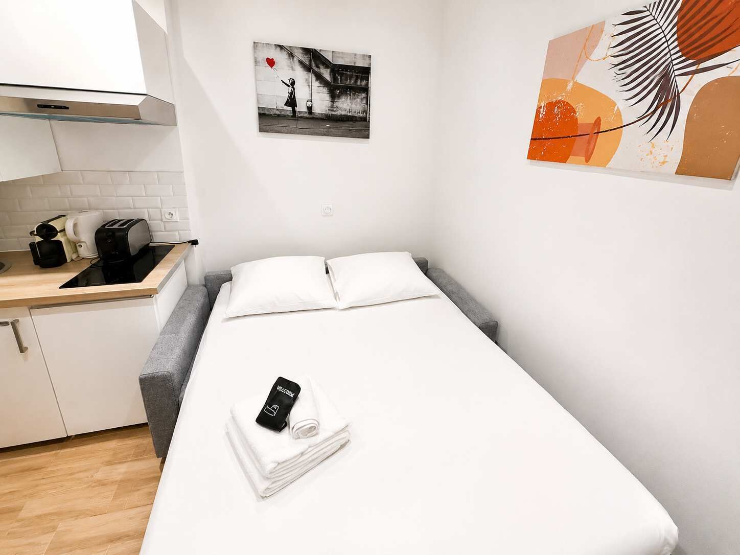 Una habitación de hotel compacta con cama, una kitchenette pequeña y una sola obra de arte en la pared.