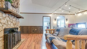 A cozy living room with a stone wall, wooden floor, and a sofa with a throw blanket. - Relaxing Cabin Retreat w/ Games! Louisbug Hideaway (Louisburg)