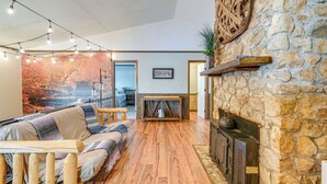 A cozy living room with a stone wall, a fireplace, and a wooden floor. - Relaxing Cabin Retreat w/ Games! Louisbug Hideaway (Louisburg)