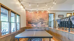A ping pong table in a room with wooden walls, large windows, and a mural of a waterfall. - Relaxing Cabin Retreat w/ Games! Louisbug Hideaway (Louisburg)