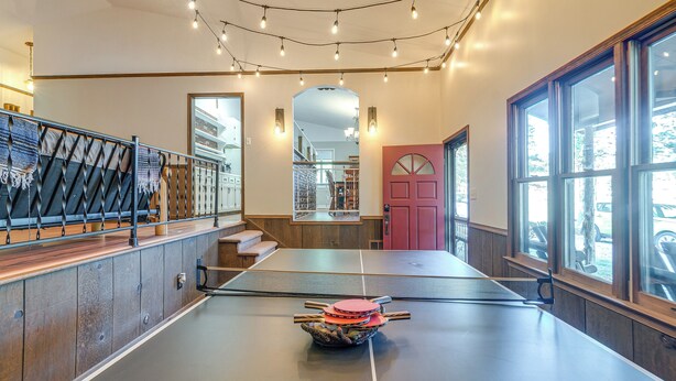 A ping pong table in a room with large windows, a mirror, and a staircase. - Relaxing Cabin Retreat w/ Games! Louisbug Hideaway (Louisburg)