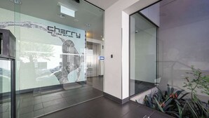 Un vestíbul modern amb una paret de vidre, un panell digital que anuncia 'cherry 165 rose street', i una petita zona amb plantes d'interior.
