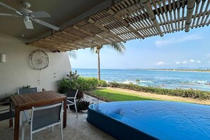A poolside area with a table and chairs, a ceiling fan, and a view of the ocean. - Dream Villa in Majahua (La Majahua)