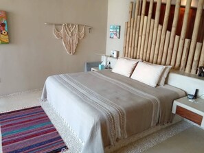 A bedroom with a bed, bedside tables, a lamp, a macrame wall hanging, and a bamboo wall panel. - Dream Villa in Majahua (La Majahua)