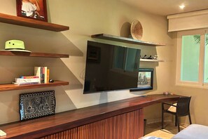 A modern living room with a large flat-screen TV mounted on the wall, wooden shelves with books and decorative items, a framed artwork, and a window with a view. - Dream Villa in Majahua (La Majahua)