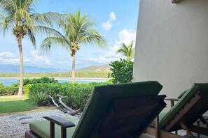 A view from a balcony with two lounge chairs facing a beach, palm trees, and a body of water. - Dream Villa in Majahua (La Majahua)