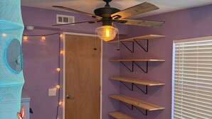 A room with purple walls, a ceiling fan, wooden shelves, a white table, and a window with blinds. - Albuquerque Gem Cozy, Central & Full of Charm (Albuquerque)