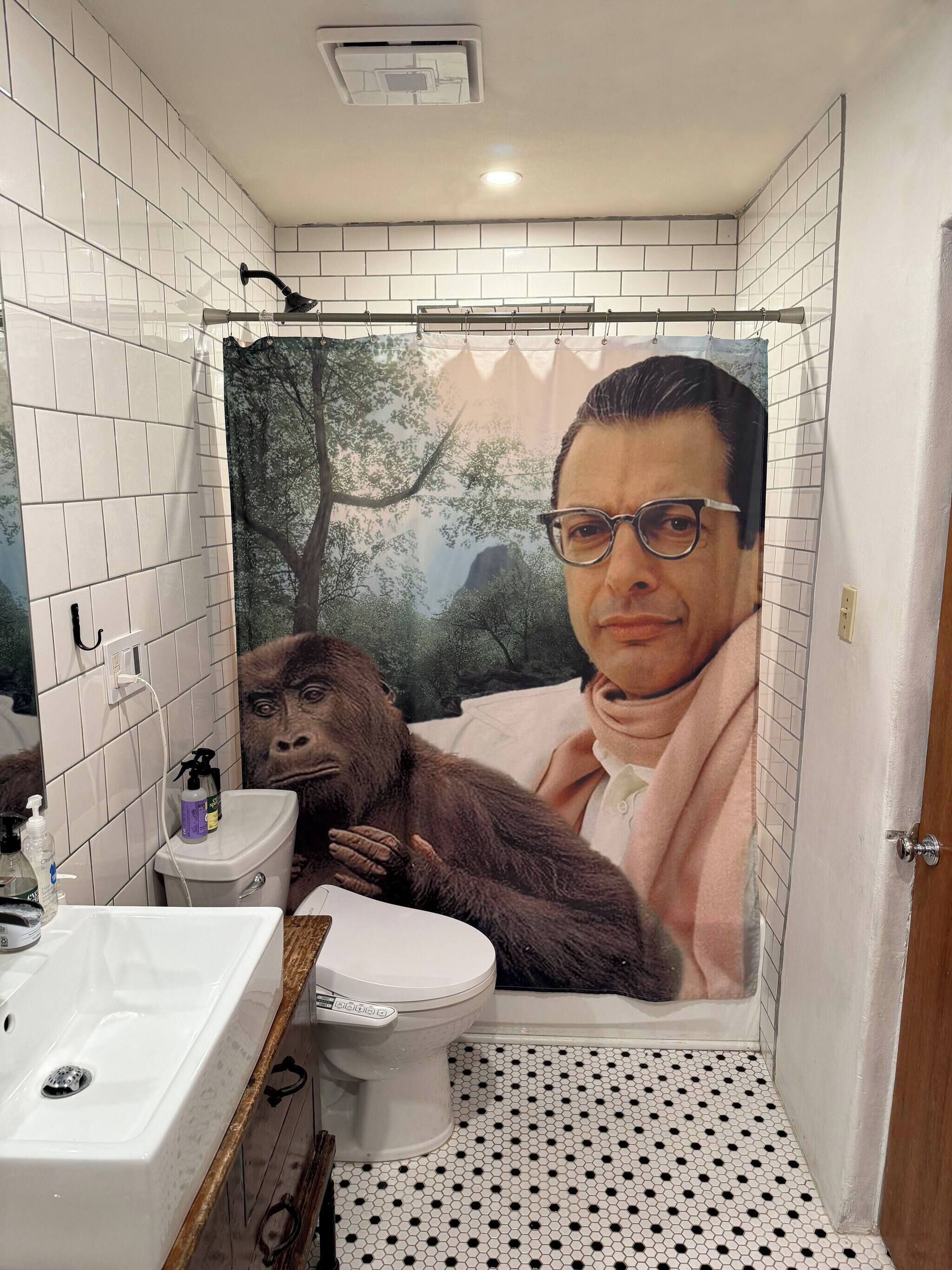 Een badkamer met witte betegelde wanden, een toilet, een wastafel en een douchegordijn met een print.
