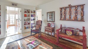 Un salon chaleureux avec un banc en bois, un tapis à motifs et une bibliothèque remplie de livres et d’objets décoratifs.