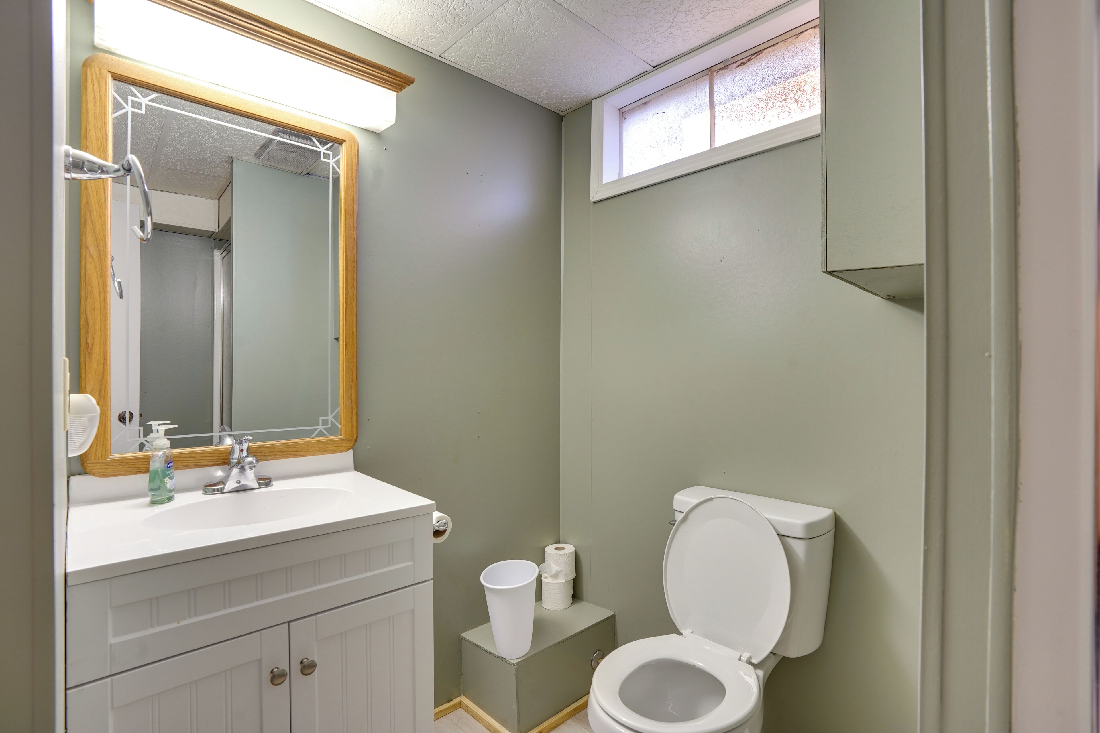 A bathroom with a white sink, a mirror with a wooden frame, a toilet, and a small window.
