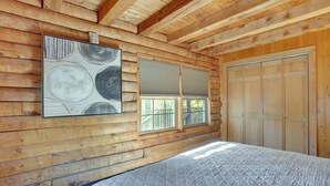 A log cabin bedroom with a bed, a window with blinds, a door, and a wall-mounted artwork. - Kentucky Lake Access! Family Log Cabin w/ Deck (Murray)