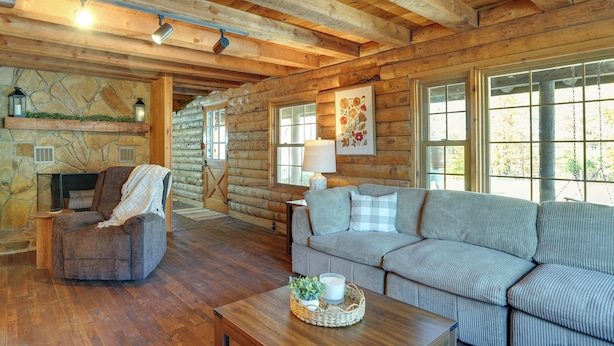 A log cabin interior with a stone fireplace, a sofa, a chair, and a wooden coffee table. - Kentucky Lake Access! Family Log Cabin w/ Deck (Murray)