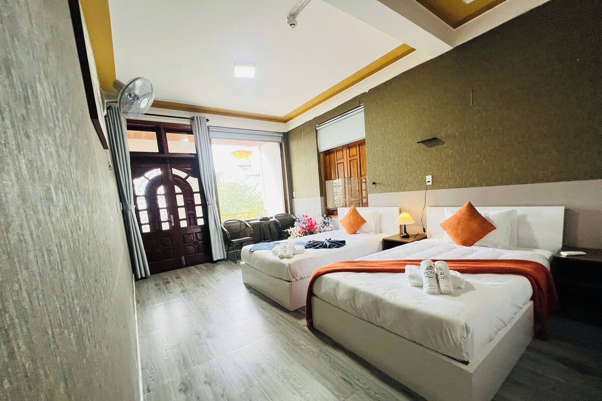 A hotel room with two beds, a sitting area, and a view of the outdoors.
