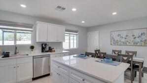 Una cocina moderna con armarios blancos, una isla central y un comedor con sillas de madera.