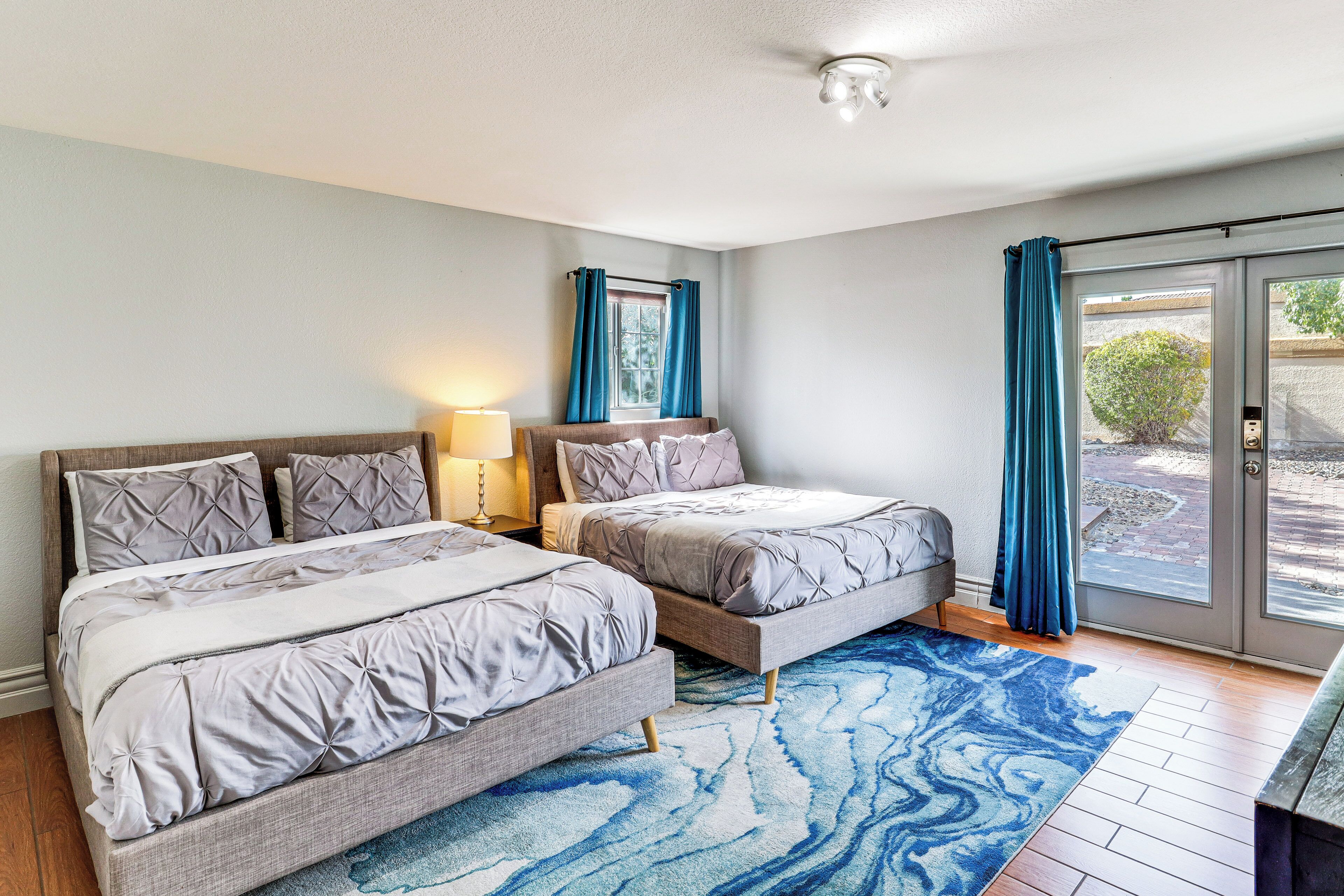 A bedroom with two beds, a large window with curtains, and a blue patterned rug.