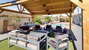 En udendørs terrasse med træmøbler, en pejseplads og en pool i baggrunden.