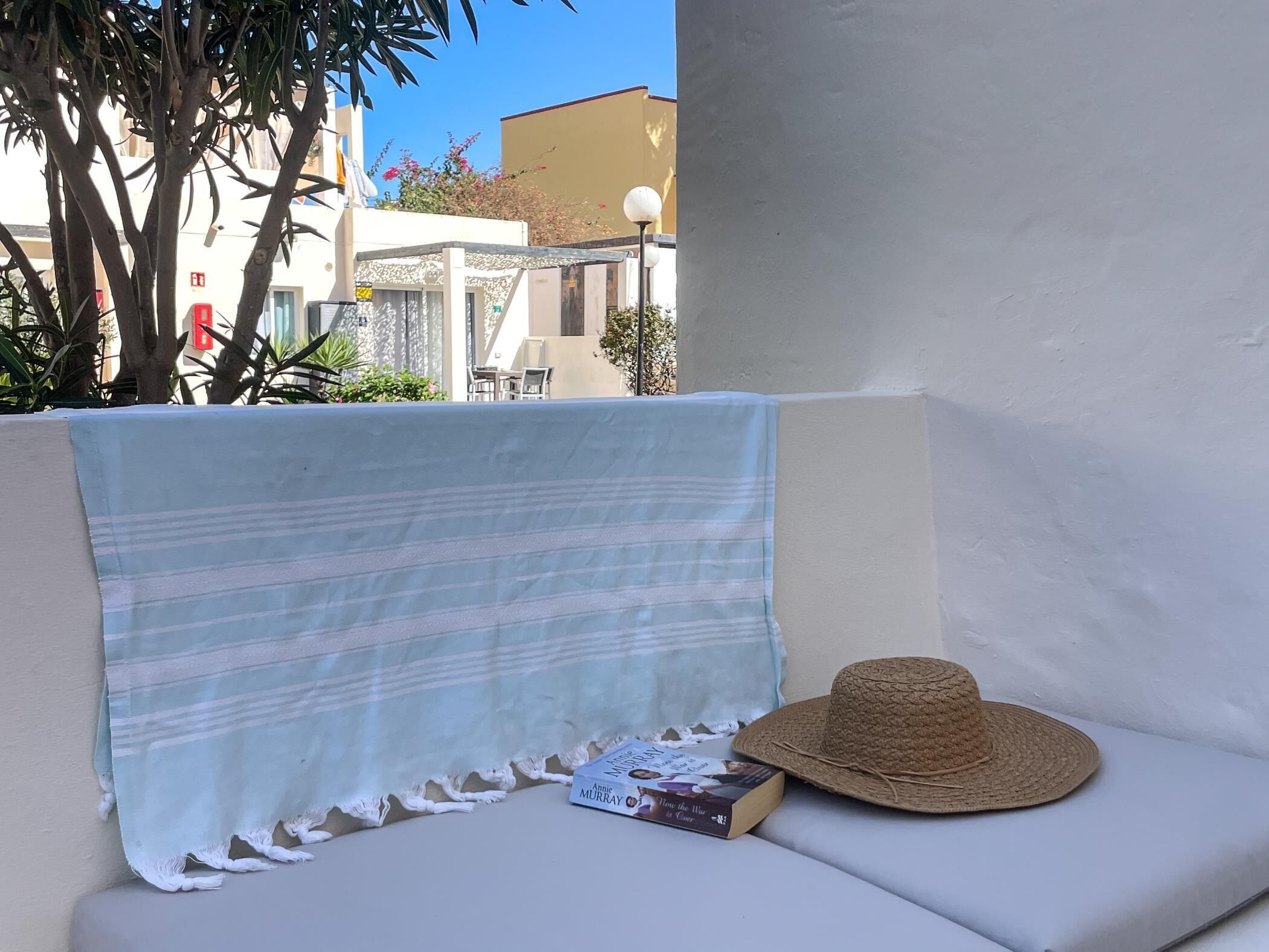 A balcony with a striped cloth, a straw hat, and a book titled 'How the War is Ours'.
