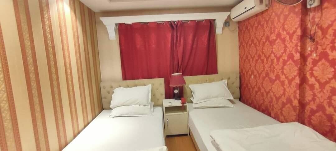 A room with two beds, a nightstand, a lamp, and a window with red curtains.