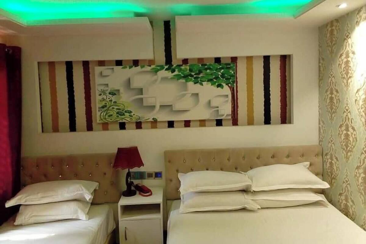 Una habitación de hotel con cabecera capitonada, mesita de noche con lámpara y un adorno en la pared.