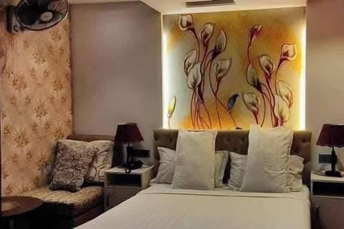 Una habitación de hotel con cama, dos mesitas de noche, un sillón y un elemento decorativo en la pared.